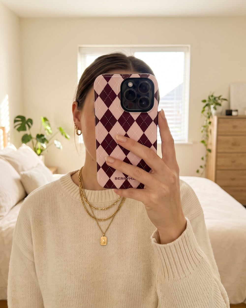 A woman taking a mirror selfie with a phone in a pink and burgundy argyle BerryMae case